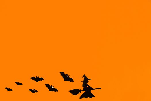 Silhouettes of a flock of bats and a witch flying on a broom made of black paper on an orange background. Halloween greeting template with copy space. Flat lay for your design. ready-made template.