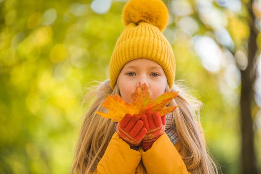 Little girl with blond hair in autumn background in yellow clothing