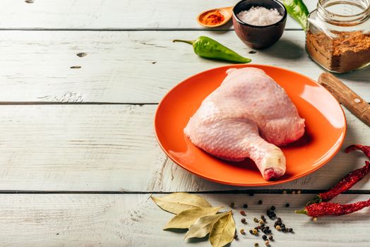 Chicken leg quarter on orange plate over wooden surface with different spices