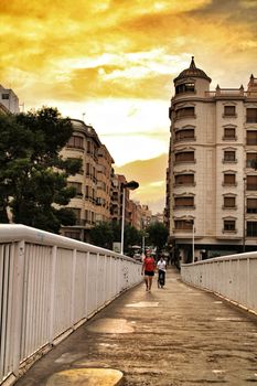 Elche, Alicante, Spain- September 12, 2018: People crossing a bridge at sunset in Elche. Beautiful buildings in the background.