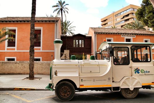 Elche, Alicante, Spain- February 14, 2019: Guided tour on Tourist train through the streets and palm groves in winter under blue sky