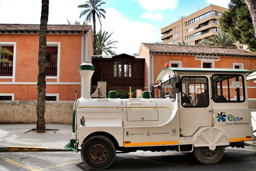 Elche, Alicante, Spain- February 14, 2019: Guided tour on Tourist train through the streets and palm groves in winter under blue sky