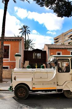 Elche, Alicante, Spain- February 14, 2019: Guided tour on Tourist train through the streets and palm groves in winter under blue sky