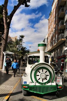 Elche, Alicante, Spain- February 14, 2019: Guided tour on Tourist train through the streets and palm groves in winter under blue sky