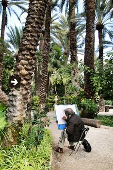 Elche, Alicante, Spain- February 14, 2019: Old senior painting and relaxing in Huerto del Cura botanical garden in Elche, Spain. Sunny day of winter.
