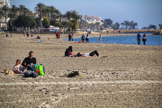 Santa Pola, Alicante, Spain- December 6, 2018: People enjoying and relaxing a sunny day of winter on the beach in Santa Pola, Spain.