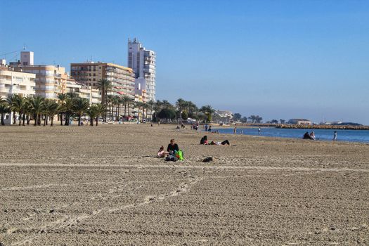 Santa Pola, Alicante, Spain- December 6, 2018: People enjoying and relaxing a sunny day of winter on the beach in Santa Pola, Spain.