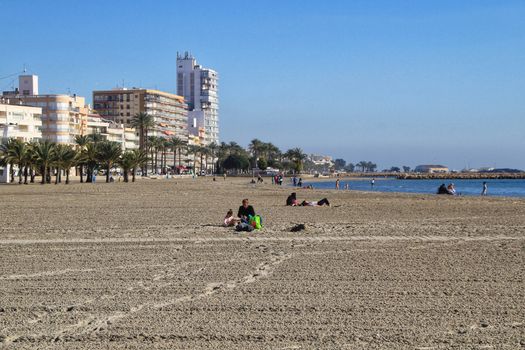 Santa Pola, Alicante, Spain- December 6, 2018: People enjoying and relaxing a sunny day of winter on the beach in Santa Pola, Spain.