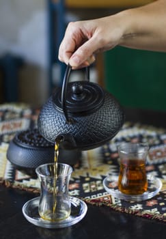 Black tea and teapot in hand, Turkish tea glasses and old iron teapot