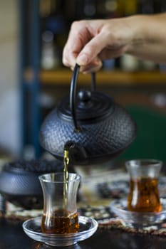 Black tea and teapot in hand, Turkish tea glasses and old iron teapot