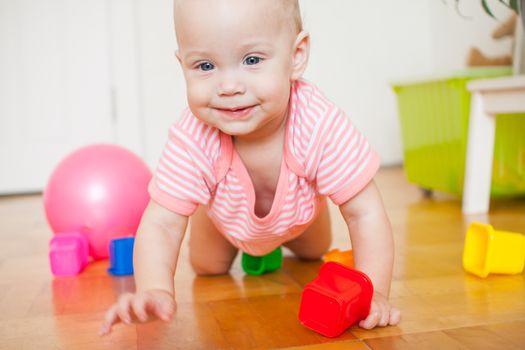 Little baby girl sitting on the floor, crawling and playing with brightly colored educational toys, pyramids