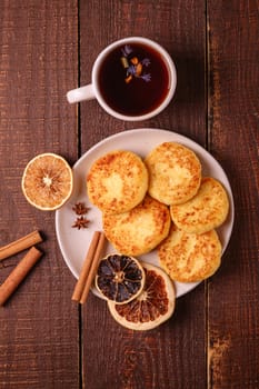 Cottage cheese fritters with hot black aromatic tea, Christmas breakfast mood with anise, cinnamon and dried citrus on wooden background, top view