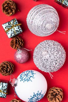 Christmas New Year composition. Gifts, fir tree cones, silver ball decorations on red background. Winter holidays concept. Flat lay, top view, copy space