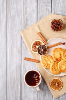 Cottage cheese fritters with hot black aromatic tea, Christmas breakfast mood with anise, cinnamon and dried citrus on wooden background, top view