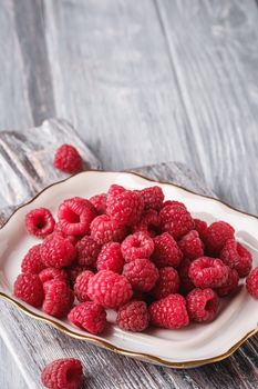 Raspberry fruits in plate on old cutting board, healthy pile of summer berries on grey wooden background, angle view macro