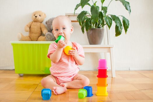 Little baby girl sitting on the floor, crawling and playing with brightly colored educational toys, pyramids