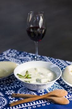 Georgian traditional food Gebjalia, cheese in milk and greens, species. Red wine and blue table cloth background.