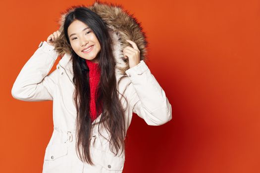 Asian woman in white hooded jacket over red background smiling