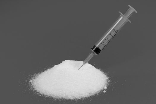 Conceptual monochrome photo of syringe and sugar emulating sugar addiction