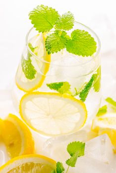 Lemonade drink in a glass: water, ice, lemon slice and mint on white background