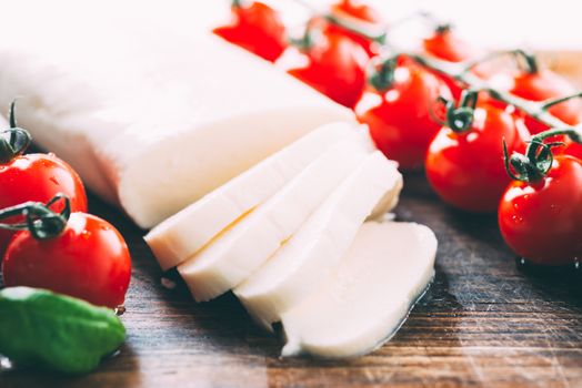 Mozzarella, cherry tomatoes and basil leaves on wooden cutting board close up