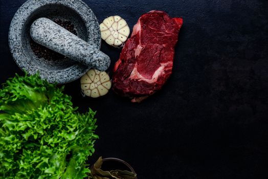 Stone mortar bowl and pestle with raw steak, garlic, bay and salad leaves