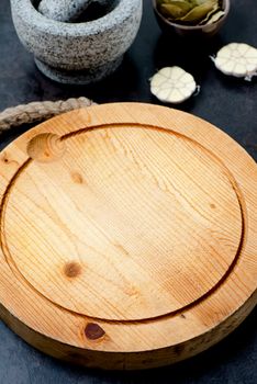 Stone mortar bowl with pestle, garlic, bay leaf and wooden cutting board on stone surface