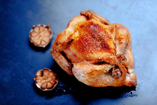Whole oven roasted chicken with garlic on stone surface