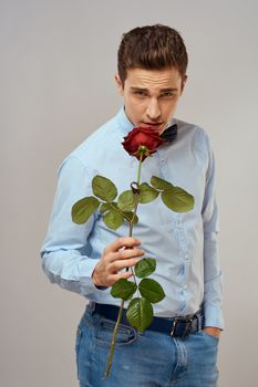 Romantic man with a red rose and in a blue shirt with a bow tie around his neck gray background. High quality photo