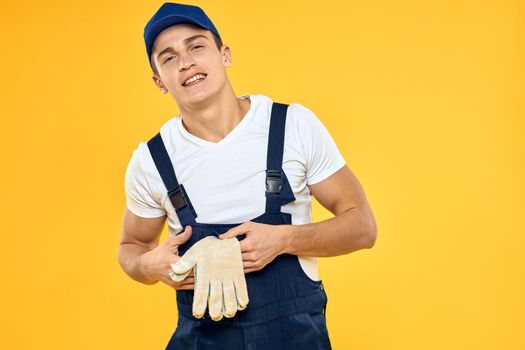 Working man in uniform of gloves rendering service yellow background. High quality photo