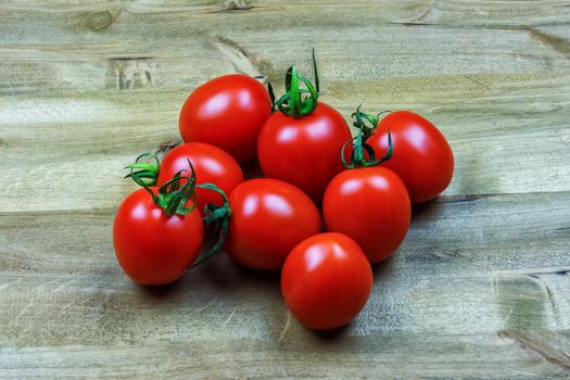 
Several small red tomatoes lie on a wooden surface