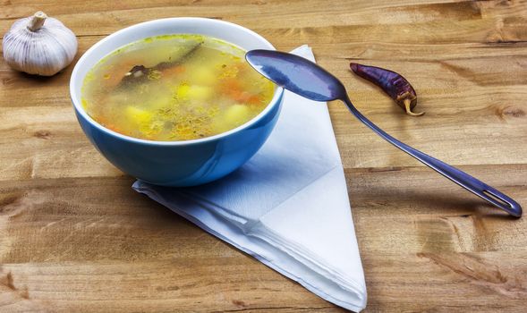 A bowl of soup with a metal spoon is on a white napkin on a table