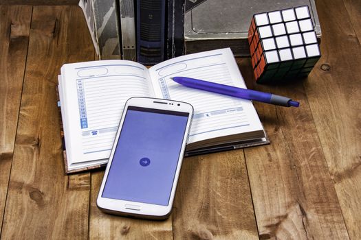 Books, diary with pen, smartphone and cube Rubik lie on a wooden surface