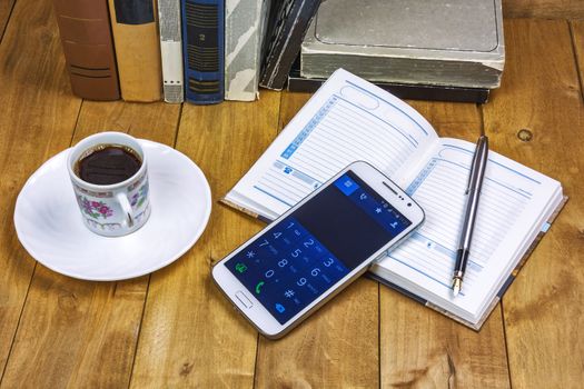 Books, a cup of coffee, a diary with a pen and a smartphone on the wooden surface
