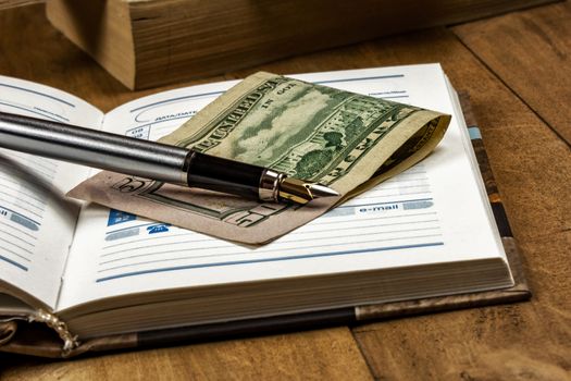 On the wooden surface is an open diary, a money note and fountain pen