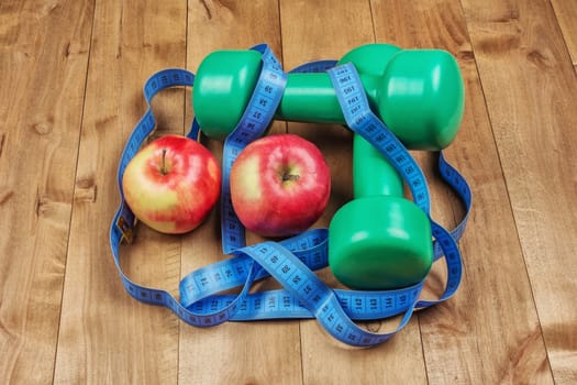 On the wooden surface are two dumbbells, apples and a centimeter