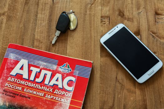 On the wooden surface is a road atlas, car key and smartphone