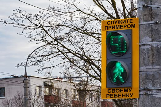 A pedestrian traffic light with a green signal and the inscription "Serve an example to your child"