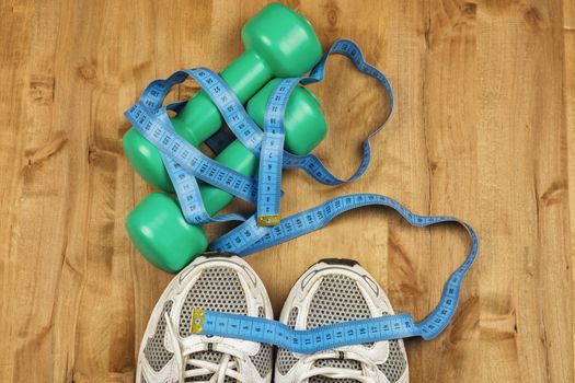 On the wooden floor are two dumbbells, white sneakers and a centimeter