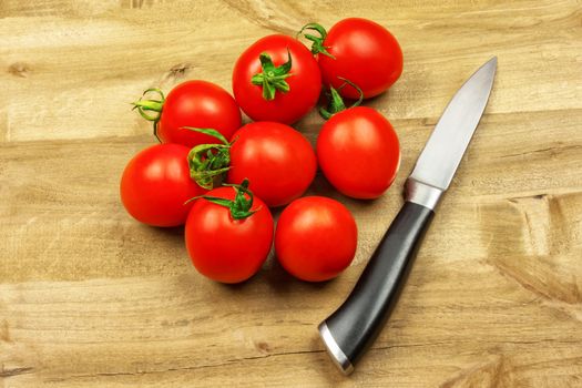 Several small red tomatoes and a knife lie on a wooden surface