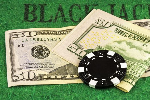 On the green cloth of the poker table there are two banknotes of 50 dollars and one black chip
