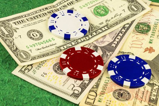 On the green cloth of the poker table is one, five and ten dollar bills and white, blue and red chips