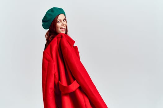 A woman holds in her hand a red coat and a dark T-shirt Green hat cropped view of a light background. High quality photo