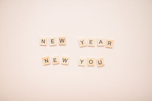 The inscription new year new you from wooden blocks on a light pink background.
