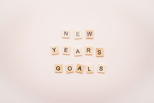 The inscription new years goals from wooden blocks on a light pink background.