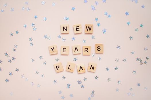 The inscription new years plan from wooden blocks on a light pink background. Silvery stars on a light pink background.