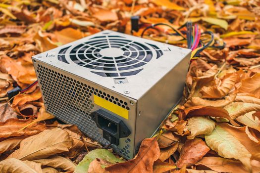 A discarded broken computer power supply lies in the autumn foliage
