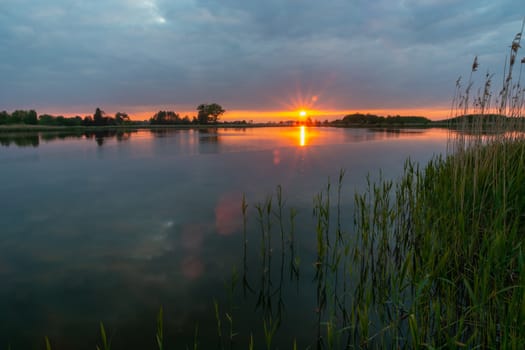 Sunset over a quiet lake with green grasses, spring evening view