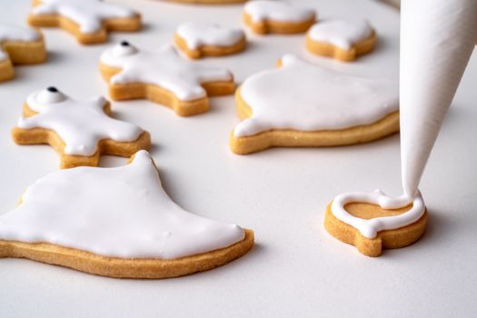 Close up of decorating cute Halloween gingerbread cookies with frosting icing cream topping bag.