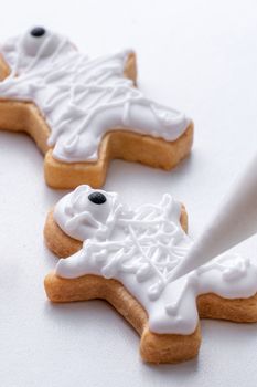 Close up of decorating cute Halloween gingerbread cookies with frosting icing cream topping bag.